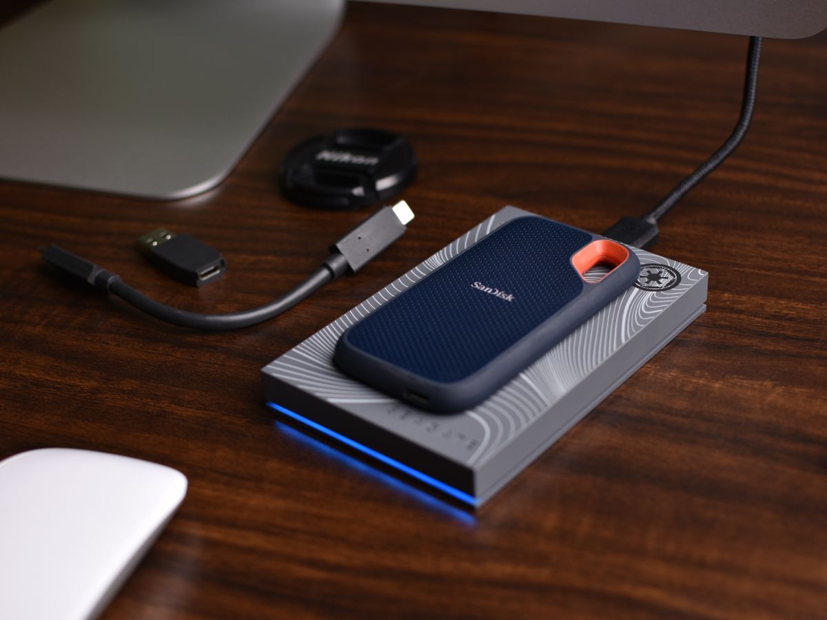 A portable SSD connected by cable on a desk beside a laptop