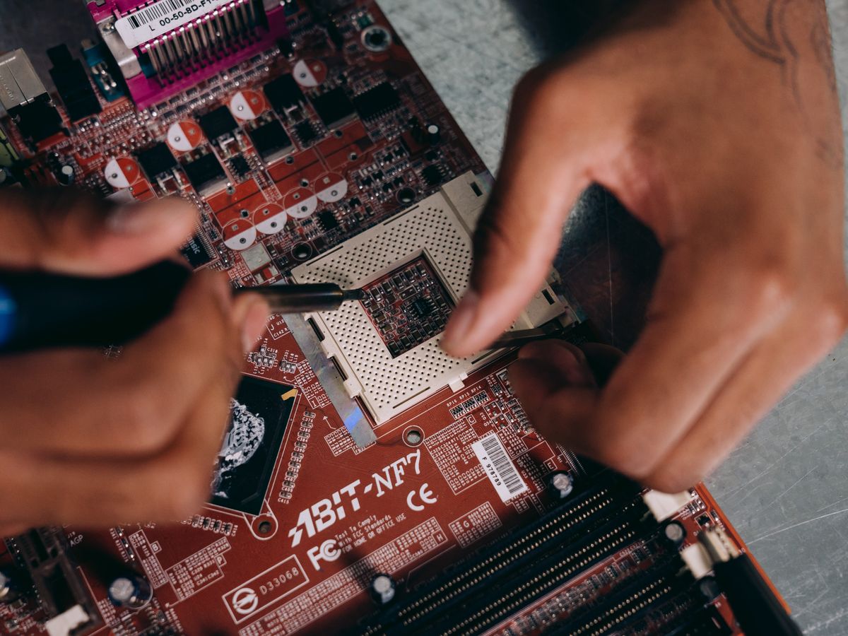 Hands using a tool to work on a computer motherboard