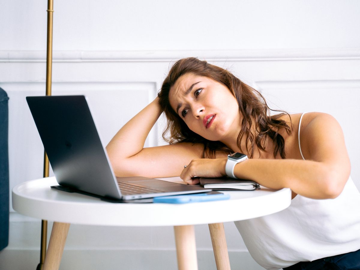 A person resting their head on a table beside an open laptop