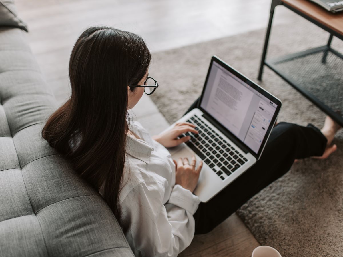 A person working on a laptop while sitting on a sofa at home