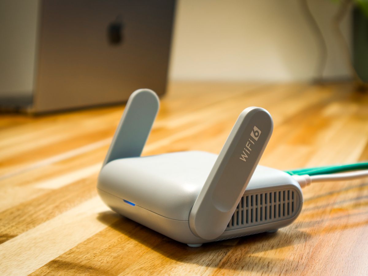 A white Wi-Fi router with folding antennas on a wooden desk